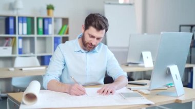 Genç yaratıcı tasarımcı ya da mimar bir bilgisayar masasında çizimlerle çalışıyor. Yakışıklı bir adam proje yapıyor. İş yerinde oturuyor, ev planı çiziyor.