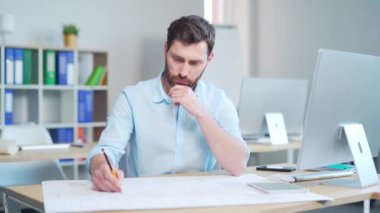 Genç yaratıcı tasarımcı ya da mimar bir bilgisayar masasında çizimlerle çalışıyor. Yakışıklı bir adam proje yapıyor. İş yerinde oturuyor, ev planı çiziyor.