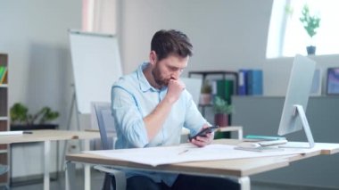 Düşünceli iş adamı ofis çalışanı modern ofiste akıllı telefon, saat ve kitap kullanır. Ciddi bir ofis çalışanı cep telefonuna bakıyor. İş yerinde, kapalı alanda. genç yönetici