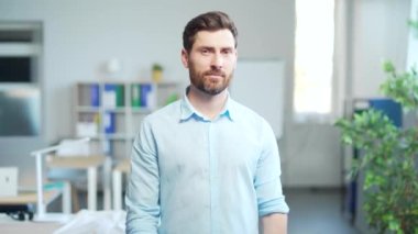 Yakışıklı, beyaz sakallı bir ofis çalışanının portresi, kameraya bakıp gülümseyen bir girişimcinin çalışanı. İşte mutlu ve neşeli bir erkek katip. Modern bir iş yerinde iş adamı.