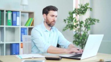 Adam iş için video izliyor. Çevrimiçi eğitim, e-öğrenme. Beyaz özgüvenli adam çalışma masasında oturuyor, dizüstü bilgisayar kullanıyor, online konferanslar dinliyor, iş yerinde notlar alıyor..