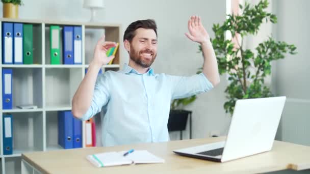 コンピュータの机に座って仕事で踊る幸せで陽気なオフィスワーカー 成功した合意の後でお楽しみください 従業員ビジネスマンインシャツハンサムな面白いひげそりマネージャーは仕事で喜びを行いました — ストック動画