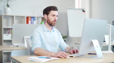 Bilgisayarda araştırma yapan odaklanmış sakallı iş adamı girişimci. Modern ofis masasında bilgisayar kullanan genç bir profesyonel. Modern teknoloji defteri üzerinde çalışan meşgul bir işçi.