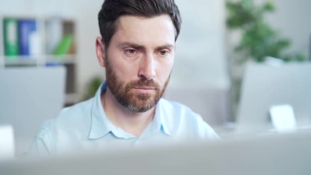 オフィスの職場でノートパソコンのコンピュータモニタの前でハンサムなひげを生やした男の肖像画を閉じる デスクに座ってるコピーライターを思いやる顔だ 人と仕事 — ストック動画