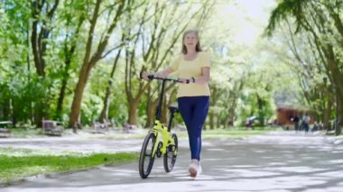 Şehir parkında bisiklet süren olgun, modern, mutlu bir kadın. Yaşlı kadın sağlıklı yaşam tarzı, bisikletle emeklilikte boş zaman. Açık havada, doğada temiz havada yürüyor.