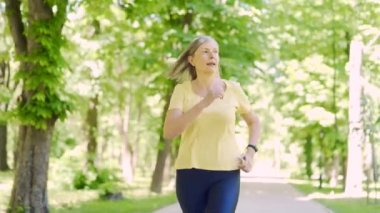 Yaşlı, gri saçlı bir kadın sabah şehir parkında koşuyor. Olgun, yaşlı kadın koşma egzersizi. Sağlıklı yaşam tarzı. Yaşlı spor koşucusu kadın antrenman yapıyor.