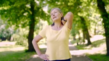Yaşlı, emekli kadın boyun ya da sırt ağrısı parkta spor yaparken. Spor egzersizleri sırasında kas ağrısı. Acı çeken olgun spor zindeliği olan bir kadın. Masaj omzumu acıtıyor.
