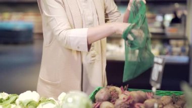 Yetişkin kadın ellerine yakın çekim yapmak ve markette sebze ya da meyve dolu eko torbaya kazmalar koymak. Markette Duran Pancar Kadın, Market Kapanışında Kullanılabilir Paket Satın Aldı