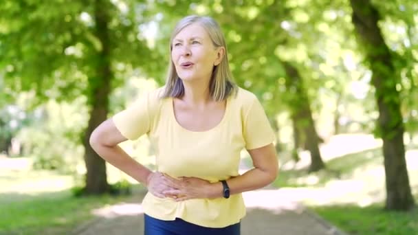 在公园外慢跑时 一位年长的女人在公园里肚子痛 成熟的女性会突然感到腹痛 跑步训练后抽筋的老跑步者 — 图库视频影像