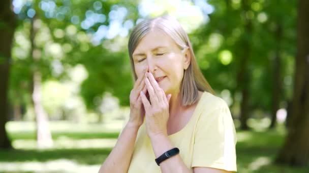 公园里患有过敏症的老年妇女流鼻涕 在树旁打喷嚏 手绢吹气 患有组织过敏症的老年妇女在公园里的室外咳嗽时打喷嚏 — 图库视频影像