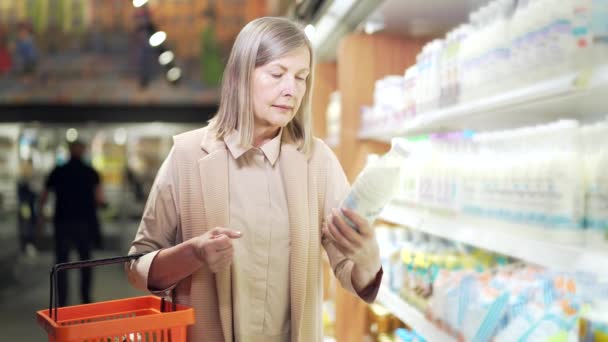 Yaşlı Yetişkin Bir Kadın Marketten Alışveriş Yaparken Süt Ürünlerini Karşılaştırıyor — Stok video