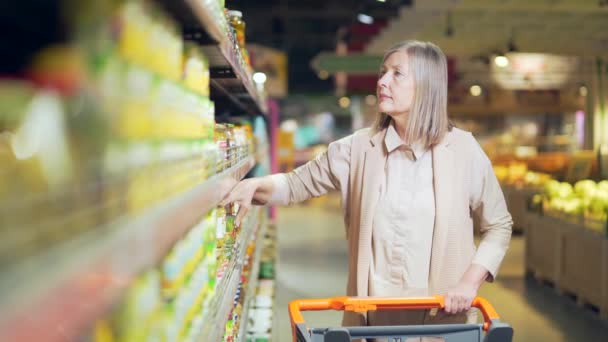 シニア引退した女性は食料品店で製品を探して選択しています 成熟した女性のスーパーマーケットの買い物客検査や棚を選ぶ 食料品市場の範囲検索商品を選ぶのは難しいですが — ストック動画