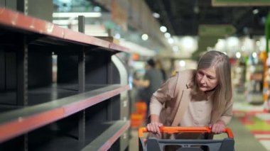 Süpermarkette son sınıf kadın alışverişçisi, boş rafların yanında bakkal. Yaşlı olgun kadın paniği satın alıp stokluyor. Biletleri tükenmiş erzak malzemeleri. Yiyecek kıtlığı.