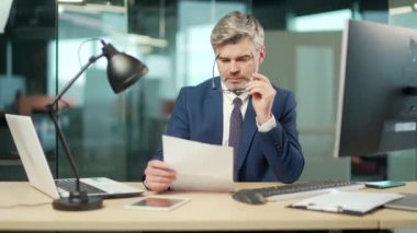 Resmi takım elbiseli ciddi bir iş adamı ofisinde oturan gri saçlı, odaklı sakallı bir iş adamı sözleşmeli bir mektup veya belge okur. Avukat bankacı iş yerinde