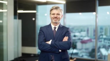 Yetişkin, gri sakallı bir iş adamının resmi takım elbiseli ve kravatlı portresi modern cam bir ofiste kameraya bakıyor. Güvenilir kıdemli iş adamı, silahlı bir girişimci.