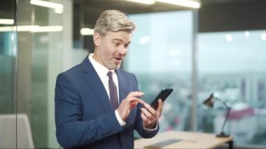 Heyecanlı, olgun iş adamı akıllı telefon sahibi, neşeli iş adamı CEO 'su. Mobil online teklif kazananı kutluyor. Zafer kazanıyor.