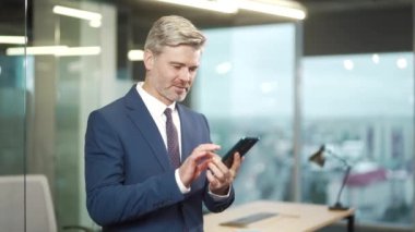 Olgun iş adamı akıllı telefonu elinde tutar tatmin edici mesajlar okur, mali raporlar alışveriş yapar, alışveriş yapar, alışveriş yapar, ödemeler yapar. CEO yönetici cep telefonu çevrimiçi ofiste iyi haberler alıyor