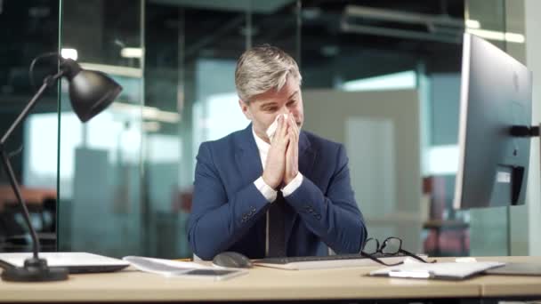 成熟的白种人男性工人患有头痛过敏 打喷嚏时流鼻涕 员工坐在办公室里工作时咳嗽感冒或流感 对一个生意人来说感觉不舒服 — 图库视频影像