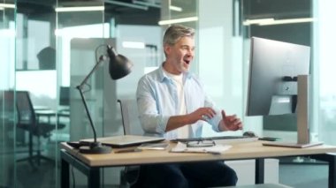 Bilgisayarda çalışan olgun sakallı işadamı çalışanı başarılı EVET Jesti 'ni kutluyor. Ilımlı ofiste çalışmak Şans Vuruşu, Büyük Kazanır. Kıdemli işçi zaferi İyi haber finansal anlaşma
