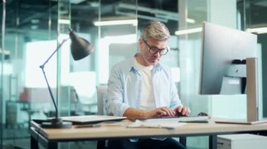 Olgun çalışanın işi bitti. Memnuniyetle ofis çalışanı arkasını yasladı. İşyerinde bilgisayar esneme işini bitirdikten sonra iş adamı dinleniyor.