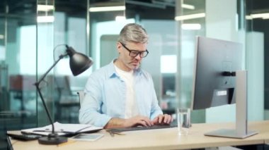 Olgun çalışanın işi bitti. Memnuniyetle ofis çalışanı arkasını yasladı. İşyerinde bilgisayar esneme işini bitirdikten sonra iş adamı dinleniyor.