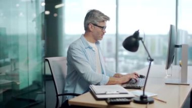 Siluet olgun, gri saçlı, kendine güveni tam bir iş adamı bilgisayar işyerinde çalışıyor modern cam ofis masasında. Odaklanmış son sınıf erkek sakallı iş adamı, çalışan.