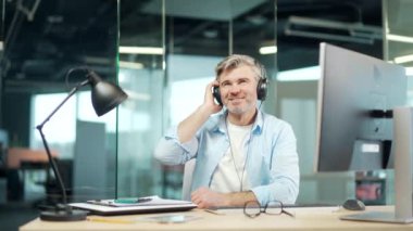 Bilgisayar masasında müzik dinleyen olgun bir işçi. Neşeli yaşlı, kır saçlı, kulaklıklı iş adamı rahatlar, dans eder ve şarkı söyler. Eğleniyorum. İş yerindeki Komik Çalışan Girişimci