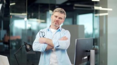 Kameraya bakan ciddi bir yaratıcı ofis çalışanının portresi. Gri saçlı kıdemli sakallı iş adamı, kendine güvenen iş adamı, gözlüklü serbest çalışan mimar, şık tasarımcı kolları çapraz