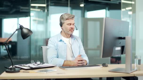 オンラインでビデオ通話で通信する成熟した灰色のビジネスマンは コンピュータのオフィスに座ってヘッドセットとウェブカメラでリモートで通信します 先輩社員が話す 相談する 会議する 会議する — ストック動画