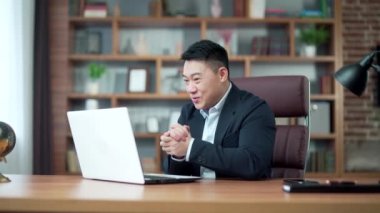 Heyecanlı Asyalı adam sevinçle bağırıyor ve el sallıyor online kumarhaneyi kazandıktan sonra dizüstü bilgisayara bakıyor ve ikramiyeyi kazanıyor. Kumar iyi haber sonuçlarını alkışlar. Kameraya bakıyorum.