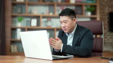 Heyecanlı Asyalı genç adam sevinçle bağırıyor ve el sallıyor online kumarhaneyi kazandıktan sonra dizüstü bilgisayara bakıyor ve büyük ikramiyeyi kazanıyor. Kumar bağımlılığı iyi bir sonucu alkışlar. Asya