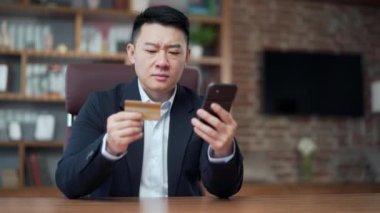 Asyalı İşadamı ofisteki cep telefonundan online ödeme hatası yapıyor. Erkek işçinin kredi kartıyla ilgili bir sorunu var. İşçi işlemi tamamlayamadı. Yeterli para yok.