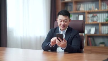 Heyecanlı Asyalı iş adamı akıllı telefonlu neşeli iş adamı CEO 'su kazandı. Mobil online teklif oyununu kazandı. Zafer kazandı.