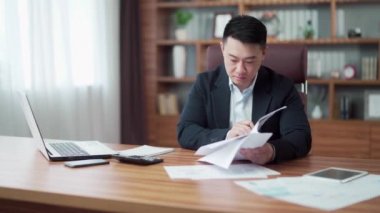 Odaklanmış Asyalı iş adamı finansal belgeleri ya da raporları inceleyen bir sözleşme imzalıyor. İş yerindeki iş yerindeki belgelerle çalışan bir işadamı. Takım elbiseli girişimci faturaları saymakla meşgul.
