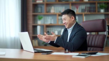 Satisfied, happy Asian businessman applauds for a Good job result online on video call using laptop computer Glad business man employee manager, boss communicates talks remotely conference meeting