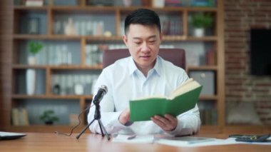 Asian teacher records online business course, uses microphone, records audio podcast, and reads audiobook, Businessman mentor works in university office. lecturer reads a book into a microphone