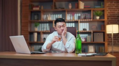 Asian businessman drinking alcohol at work in the office. Alcoholism. employee entrepreneur fails, man in despair, sitting late in workplace at computer desk, depressed, hopeless with grief. Asia