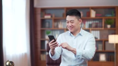 Excited asian business man hold smartphone overjoyed businessman worker, employee winner celebrate mobile online bid game win victory success receive read good news on cell phone expression at office
