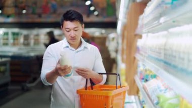 asian man doing daily shopping in grocery store in the supermarket uses a checklist list reminder. Male customer, purchaser Buys milk near the dairy department, pick and puts the goods in the basket
