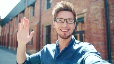 POV young man communicates online by video call on the front camera of a smartphone outdoors. outside. smart phone webcam view screen. Happy student guy waves his hand and speaks point of view