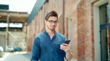 Young handsome man walks down the city street uses a smartphone. Happy, trendy, stylish guy tourist traveling using gps navigation online phone maps to plan a route on the urban background outside