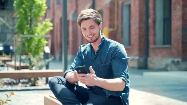 Happy Young Guy Student Casual Denim Shirt Using Smartphone While — Vídeo de Stock