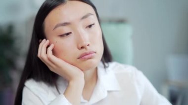 Bored sleepy Asian office worker sitting at work workplace at computer desk leaning on hand. Tired woman. Exhausted young Businesswoman employee. Portrait Depressed, unhappy, workless female manager