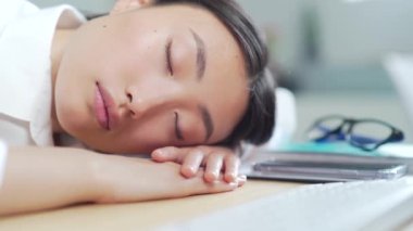 Yorgun Asyalı iş kadını ofis çalışanı ya da iş yerinde uyuyan tezgahtar. Aşırı yüklenmiş iş kadını çalışanı masaüstünde uyuyakalıyor. İş yerindeki masaüstünde çok çalışan yorgun bir kadın. Asya