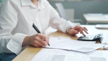 Kırpılmış eller, iş yerindeki belgelerle çalışan genç muhasebeci bayanı kapatıyor. Hesaplama mali raporu. Hesap makinesi kullanıyor. Bayan işçi girişimci evrak işleriyle meşguldür.