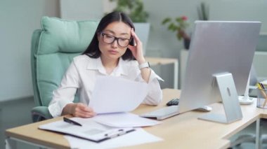 Difficult asian woman employee to deal with paperwork. documents. Stressed businesswoman confused by mistake, looking at camera through papers. bookkeeper, booker vaguely, dimly at work in office