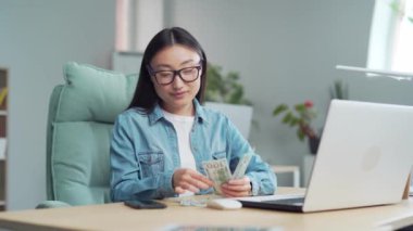 young asian woman counting cash dollar bills at workplace in office. Satisfied employee Freelancer entrepreneur income or salary in envelope income profit Win online award for work done good job. Asia