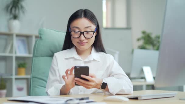 Happy Asian Business Woman Employee Entrepreneur Uses Smartphone Sitting Workplace — Vídeo de stock