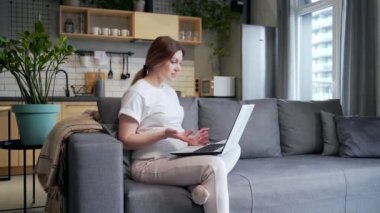 young pregnant business woman works remotely make a meeting, conference, briefing or interview online by video call using webcam laptop computer. Female freelancer is busy at home during pregnancy