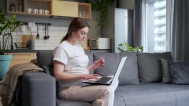 pregnant woman shopping online on the Internet store. Female makes a payment using a laptop computer uses plastic credit card while sitting at home on the sofa. pays for purchases